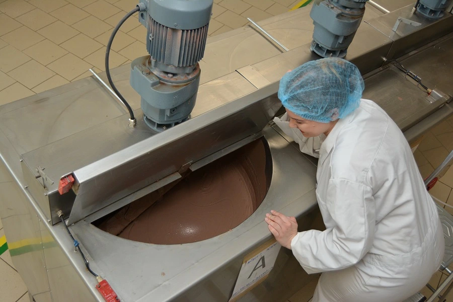 female worker in white coat with liquid chocolate in factory